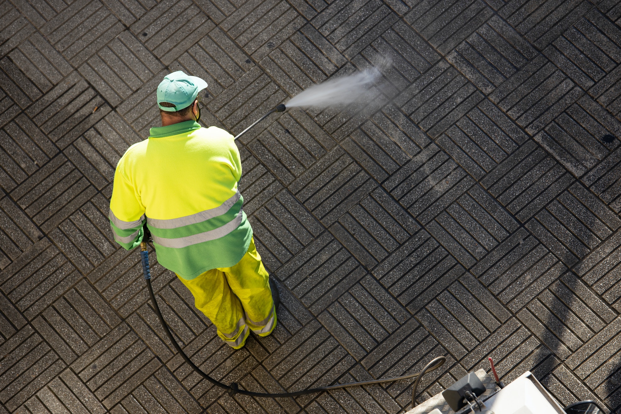 Worker cleaning a street sidewalk with high pressure water jet machine